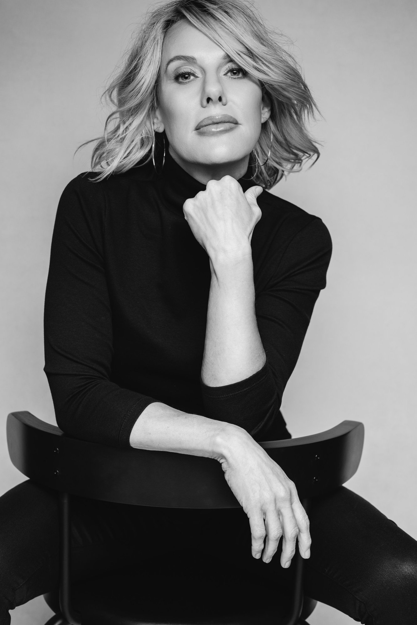Carissa A. Jakobe seated backwards on a chair, chin on her hand, in a black-and-white studio portrait
