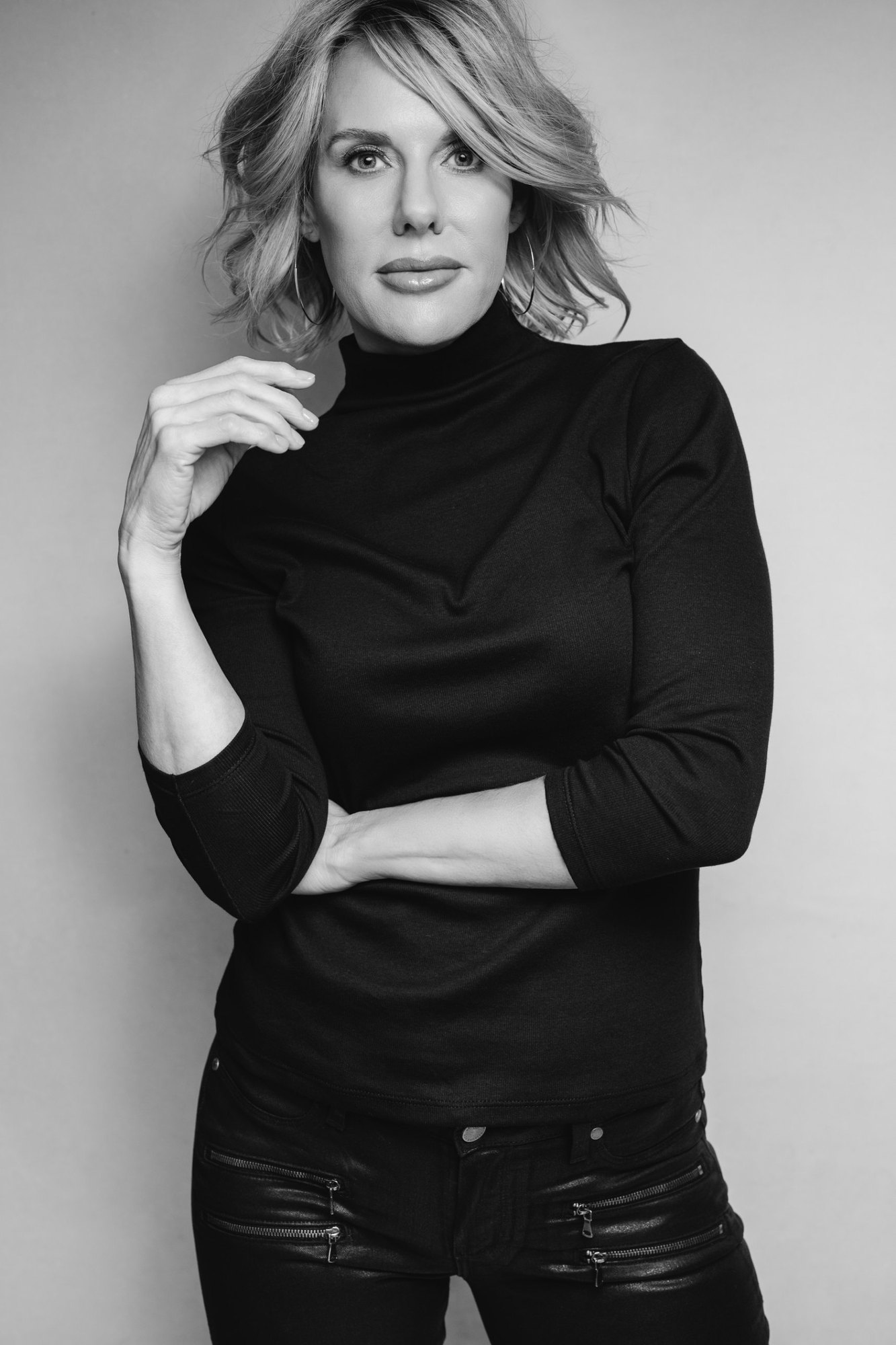 Carissa A. Jakobe, standing with arms folded and a hand at her chin, in a black-and-white studio portrait