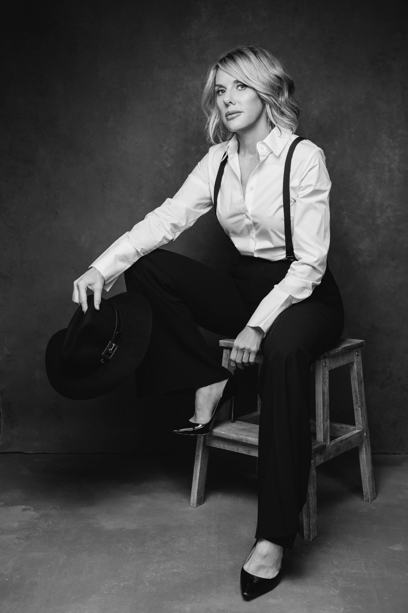 Carissa A. Jakobe, seated on a stool holding a hat, in a black-and-white studio portrait